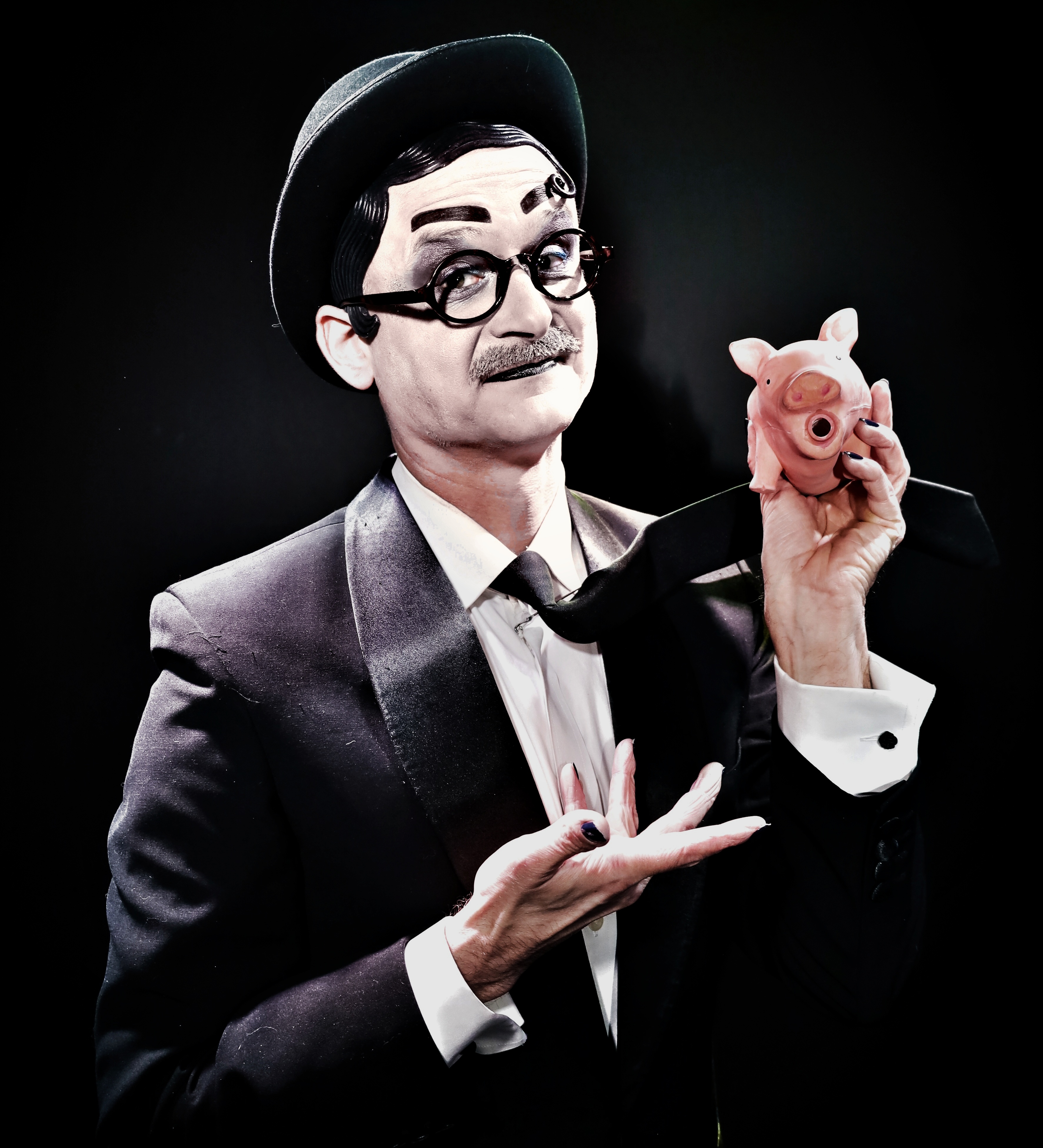 Enrico Touché wears a tuxedo and holds a rubber pig